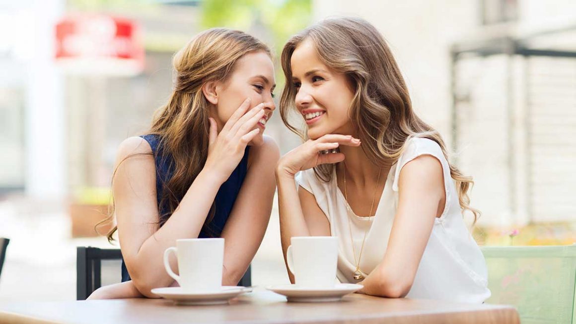 deux femmes à une table d'un café se disent un secret pour représenter l'étude sur l'amitié réalisée par Gleeden